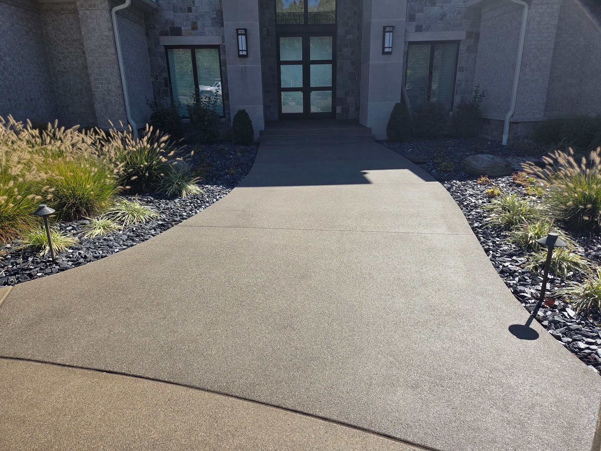 Wide-angle shot of a perfectly smooth polished stamped concrete driveway and patio at a modern custom home — slate grey finish with decorative border pattern, soft natural daylight highlighting the flawless surface texture